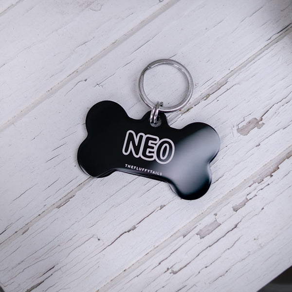 Svart hundbensformad ID-bricka med namnet Neo på en vit trähylla