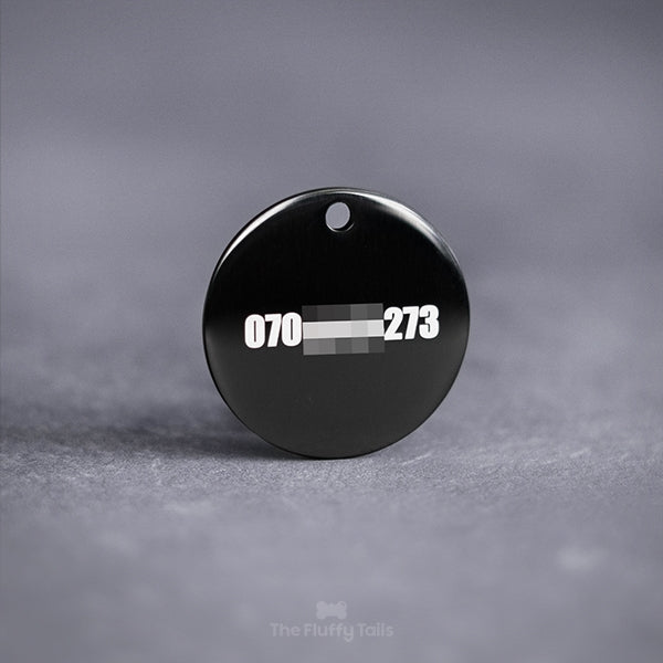 Baksida på en svart, rund namnbricka för hund och katt, graverad telefonnummer