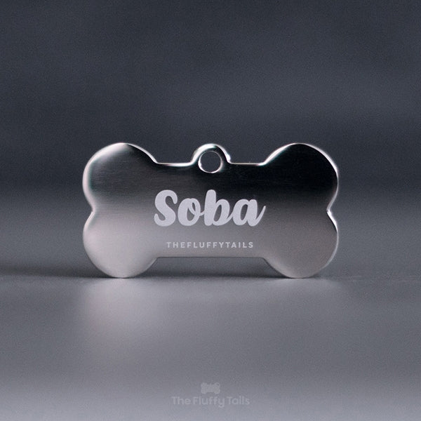 Silvrig, hundbensformad namnbricka, graverad med namn skriven med typsnitt i skrivstil