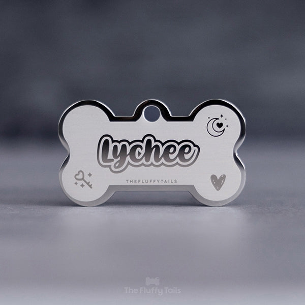 Hundbensformad, silvrig namnbricka med ikoner med måne, hjärta, nyckel med hjärtform och glitter, hundens namn i skrivstil