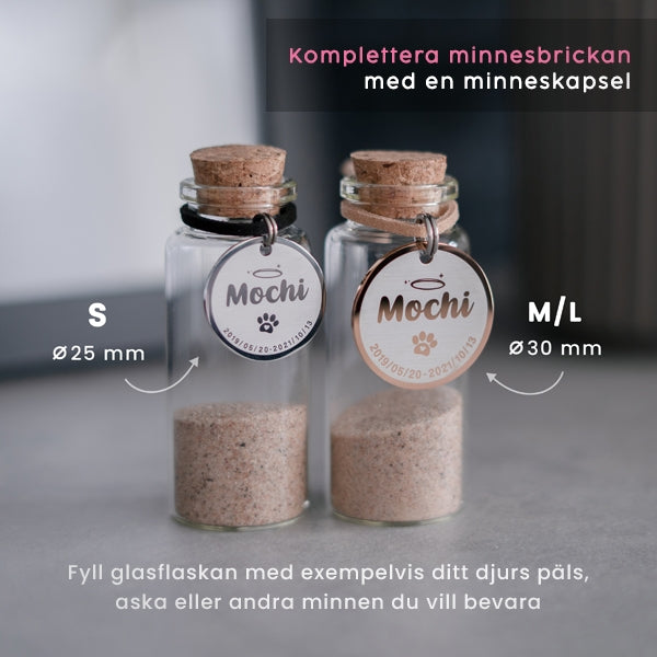2 glasflaskor (minneskapslar) med runda minnesbrickor (en silver och en roséguld) på flaskhalsen