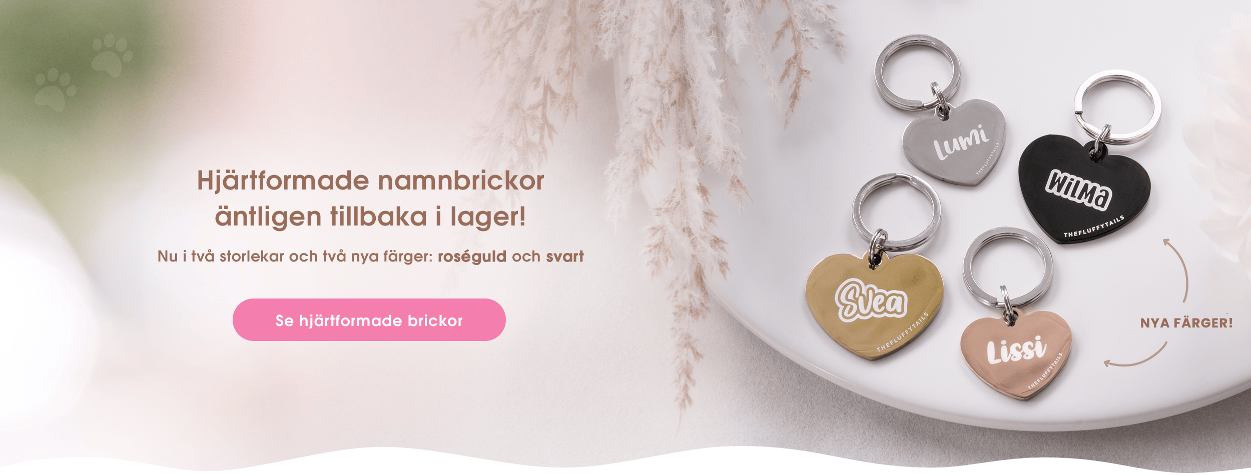 Banner med fyra hjärtformade namnbrickor i svart, silver, roséguld och guld samt text om nyheter: XS-storlek och hjärtbrickor i nya färger