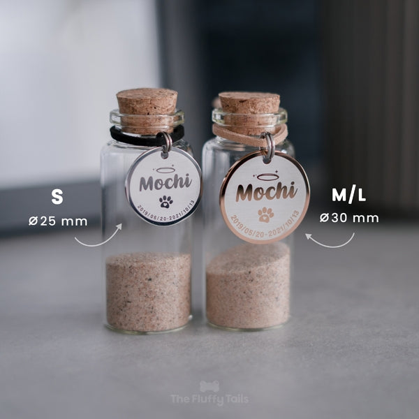 Två glasflaskor, minneskapslar med varsin minnesbricka "Gloria" från The Fluffy Tails, i storlek S silver, och M/L roséguld hängandes runt flaskhalsen