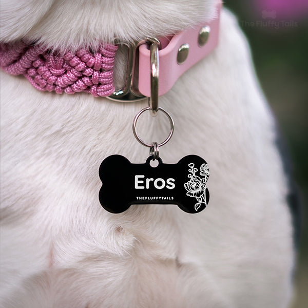 Närbild på vit hund i rosa hundhalsband med en svart hundbensformad ID-bricka med pioner på