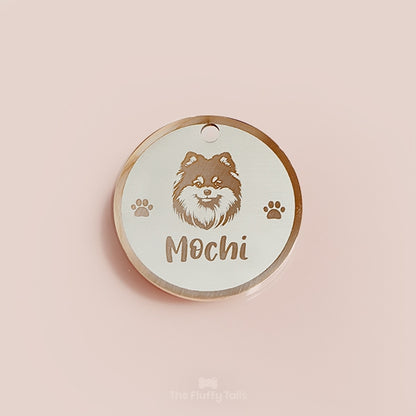 Rund egendesignad ID-bricka i roséguld med pomeranianhund, två tassar på varje sida och hundens namn 