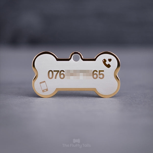 Guldig, hundbensformad namnbricka med telefonnummer, ikon på 2 telefoner och ett hjärta på en ljus bakgrund