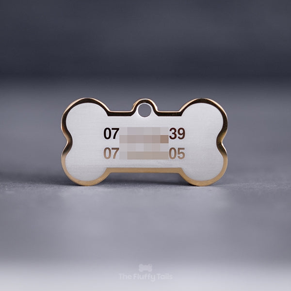 Guldig, hundbensformad namnbricka med 2 telefonnummer på en ljus bakgrund