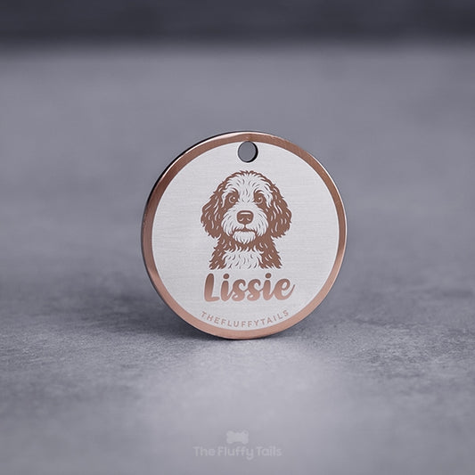 Rund namnbricka, id-bricka, i roséguld med ljus bakgrund, graverad med bild på en portugisiskt vatten hund och hundens namn i skrivstil