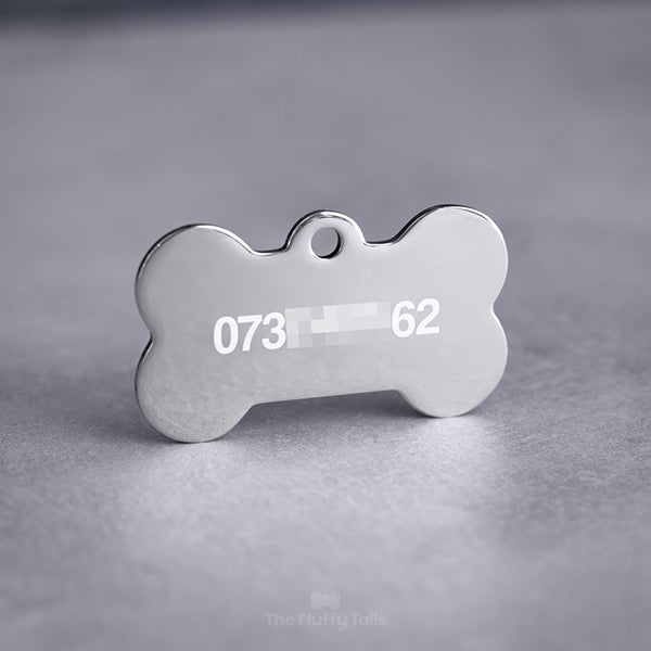 Baksidan på en silvrig, hundbensformad ID-bricka, graverad med telefonnummer