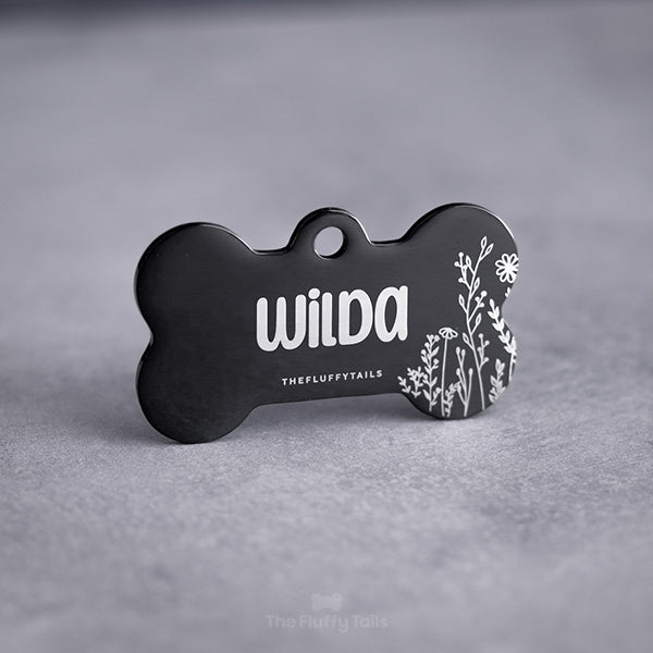 Svart, spegelblank, hundbensformad ID-bricka graverad med somrig design, vita växter och namn