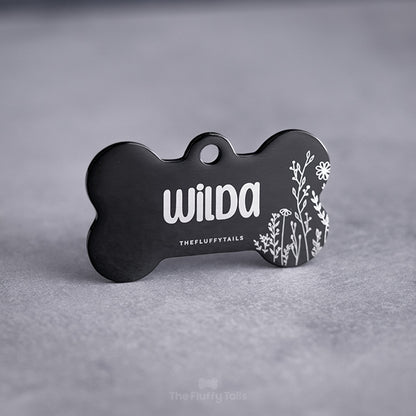 Svart, spegelblank, hundbensformad ID-bricka graverad med somrig design, vita växter och namn