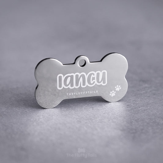 Spegelblank, silvrig, hundbensformad id-bricka graverad med namn med enkel kontur och vita tassavtryck