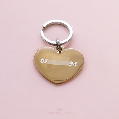 Baksidan av en guldig, hjärtformad ID-bricka, namnbricka, graverad med telefonnummer