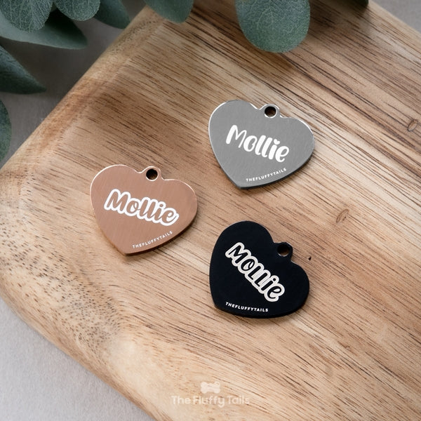 Hjärtformade namnbrickor i silver, roséguld och svart med personlig gravyr i olika typsnitt.