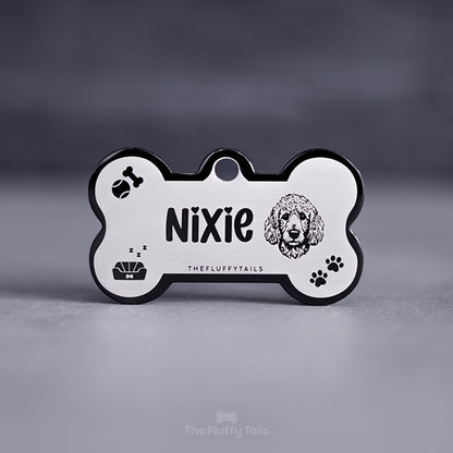 Svart namnbricka, ID-bricka med personlig gravyr och egen design, designad med ikoner av en pudel, tennisboll, tuggben, hundbädd och tassavtryck.