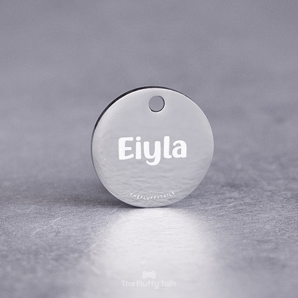 Rund silvrig namnbricka, graverad med hundens namn i ett handskrivet typsnitt