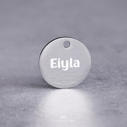 Rund silvrig namnbricka, graverad med hundens namn i ett handskrivet typsnitt