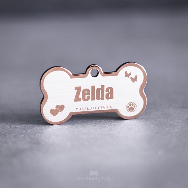 Hundbensformad namnbricka av rostfritt stål i färgen roséguld med egen design och gravyr med fjärilar, hjärtan, tassavtryck och hundens eller kattens namn.