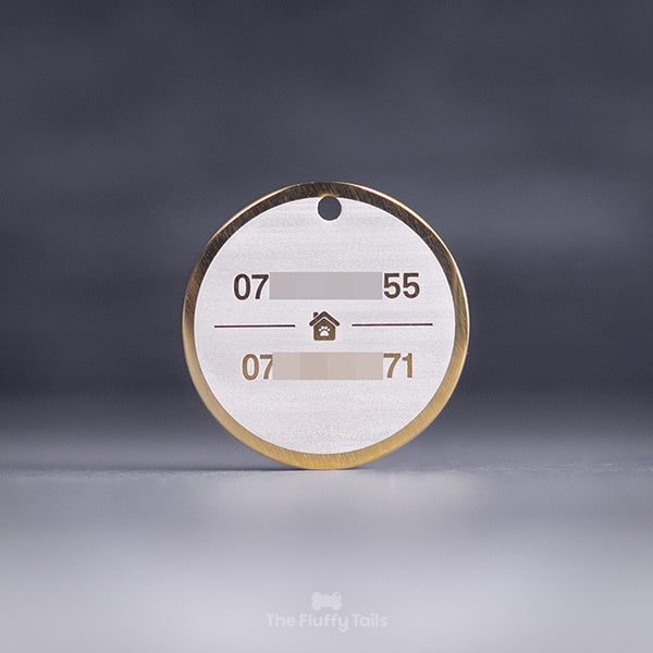 Rund, guldig namnbricka för hund och katt, graverad med två telefonnummer och ett hus i mitten.