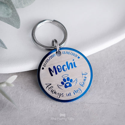 Rund, blå nyckelring, minnesbricka med personlig gravyr av hundens namn och datum, tassavtryck med hjärta och vingar