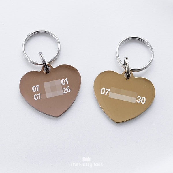 Baksidan på två hjärtformade namnbrickor, den ena i guldig färg graverad med ett telefonnummer och den andra i roséguld graverad med två telefonnummer. Passar hundar och katter.