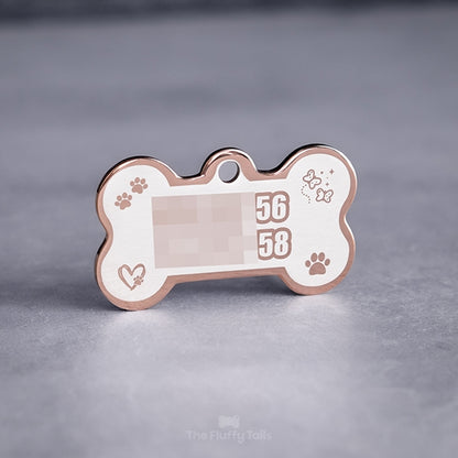 Baksidan på en roséfärgad, hundbensformad namnbricka av rostfritt stål för hundar och katter, graverad med två telefonnummer till ägarna med kontur och fyra ikoner av tassar, fjärilar med glitter och hjärta med tassavtryck inuti.