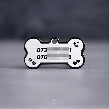 Svart hundbensformad namnbricka av rostfritt stål, graverad med två telefonnummer, tassar, dubbelhjärtan och en telefonlur