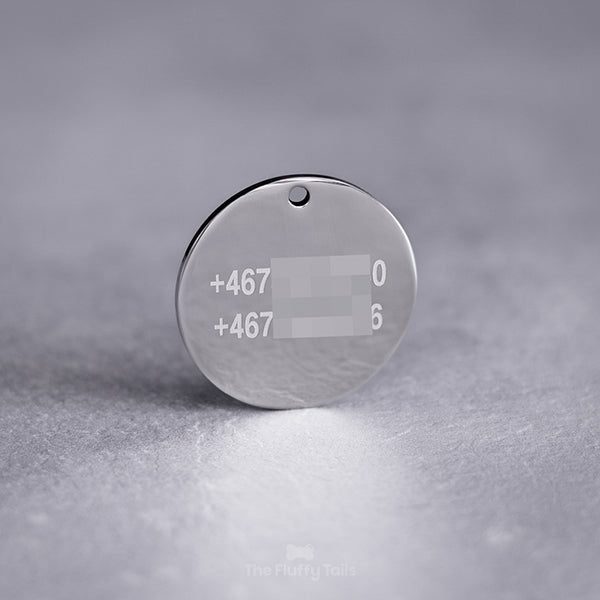 Baksidan på en rund, silvrig ID-bricka av rostfritt stål, graverad med två telefonnummer