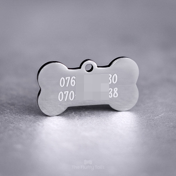 Baksidan på en silvrig hundbensformad ID-bricka, namntag för hund och katt. Tillverkad av rostfritt stål med spegelpolering. Graverad med två telefonnummer.