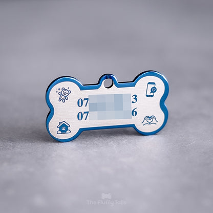 Blå, hundbensformad namnbricka av rostfritt stål med spegelpolering , graverad med två telefonnummer och ikoner av nallebjörn, telefon, hus och handhjärta.