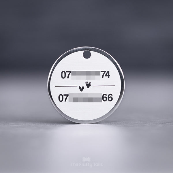 Rund, silvrig namnbricka av rostfritt stål, graverad med två telefonnummer till hundägarna och två handritade hjärtan i mitten, passar både hund och katt
