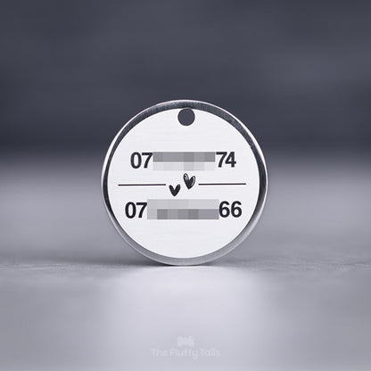 Rund, silvrig namnbricka av rostfritt stål, graverad med två telefonnummer till hundägarna och två handritade hjärtan i mitten, passar både hund och katt