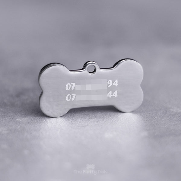 Silvrig, hundbensformad namnbricka av rostfritt stål, graverad med två telefonnummer uppdelade på två rader