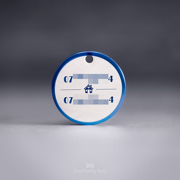 Blå, rund namnbricka av rostfritt stål med personlig gravyr och egen design. Namnbrickan är graverad med två telefonnummer till ägarna, uppdelade på två rader med ett hus i mitten med ett hjärta på fasaden.