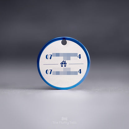 Blå, rund namnbricka av rostfritt stål med personlig gravyr och egen design. Namnbrickan är graverad med två telefonnummer till ägarna, uppdelade på två rader med ett hus i mitten med ett hjärta på fasaden.