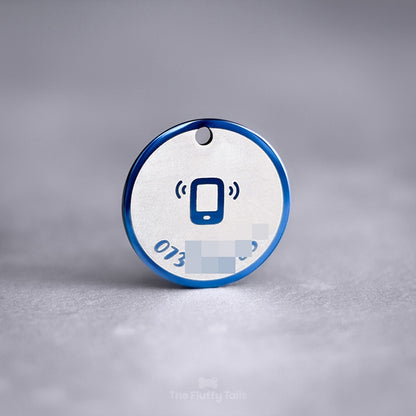 En blå, rund ID-bricka av rostfritt stål med spegelpolering som skiftar fint i ljuset. ID-brickan är graverad med ett telefonnummer längs namnskyltens runda form. I mitten av namnbrickan har en ikon på en ringande telefon graverats. Passar både hundar och katter.