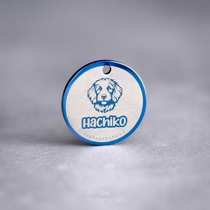 Blå, rund namnbricka av rostfritt stål med egen design. Namnbrickan är graverad med hundens namn och motiv på en hund av rasen goldendoodle.