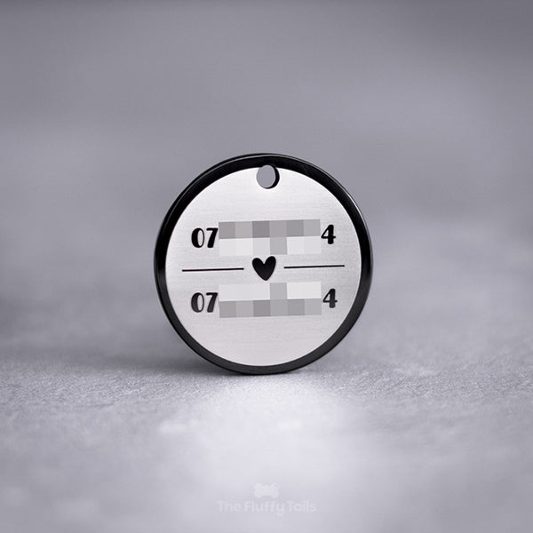 Baksidan på en exklusiv svart, rund namnbricka av rostfritt stål graverad med två telefonnummer uppdelade på två rader med ett hjärta emellan