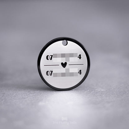 Baksidan på en exklusiv svart, rund namnbricka av rostfritt stål graverad med två telefonnummer uppdelade på två rader med ett hjärta emellan