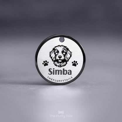 Svart, rund namnbricka av rostfritt stål graverad med egen design föreställande en goldendoodle hund och två tassar på varje sida av hunden.
