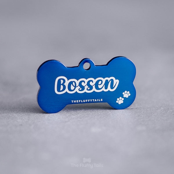 Hundbensformad namnbricka av rostfritt stål med högblank yta till hund, graverad med hundens namn i enkel kontur och två tassar.