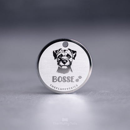 Rund silverfärgad hundbricka med graverat porträtt av en hund och namnet “Bosse” tillsammans med små tassavtryck på ljus bakgrund.