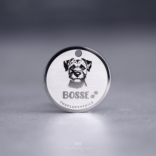 Rund silverfärgad hundbricka med graverat porträtt av en hund och namnet “Bosse” tillsammans med små tassavtryck på ljus bakgrund.