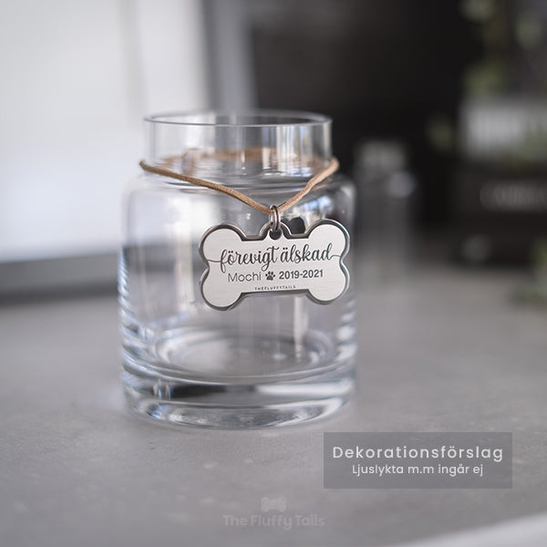 Silvrig hundbensformad nyckelring, minnesbricka med texten förevigt älskad, till minne av ett husdjur, hund eller katt som har gått bort. Hänger på en glasljuslykta.