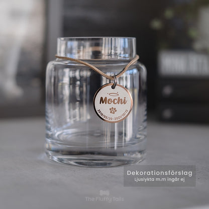 Rund minnesbricka i roséguld av rostfritt stål, graverad med djurets namn, tassavtryck och datum. Kan användas som nyckelring. Till minne av ett husdjur, hund eller katt som har gått bort. Hänger på en glasljuslykta.