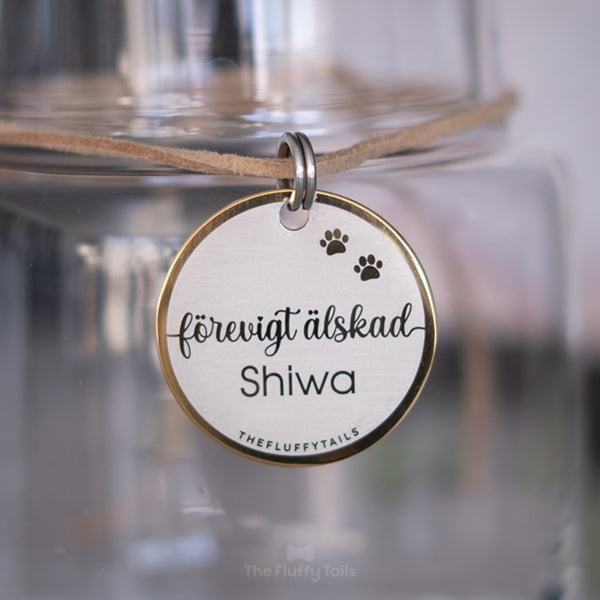 Rund, guldig nyckelring av rostfritt stål med texten "Förevigt älskad", djurets namn och tassavtryck. Till minne av ett husdjur som har gått bort