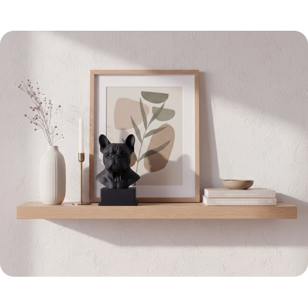 Interiörbild för inspiration med en svart hundskulptur i 3D av hundrasen fransk bulldog, inredd i minimalistiskt och skandinaviskt stil tillsammans med en lång, guldig ljusstake, tavla i ek, vit hög vas med torkade växter och en keramik skål på två böcker