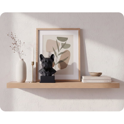 Interiörbild för inspiration med en svart hundskulptur i 3D av hundrasen fransk bulldog, inredd i minimalistiskt och skandinaviskt stil tillsammans med en lång, guldig ljusstake, tavla i ek, vit hög vas med torkade växter och en keramik skål på två böcker