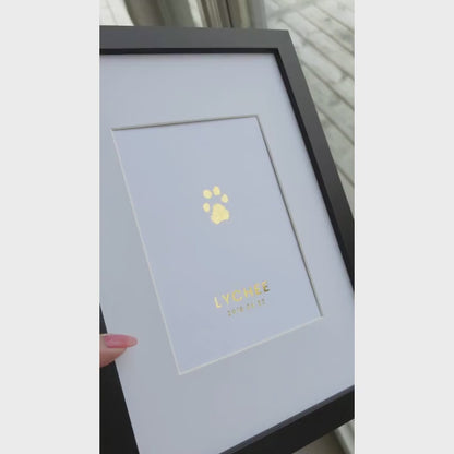 Video som visar en inramad TassPrint med tassavtryck folierat i guld. Tavlan vinklas i dagsljus för att visa foliens reflekterande effekt