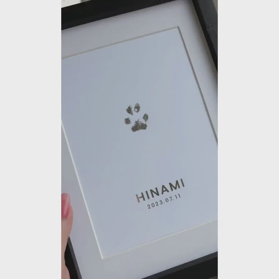 Video som visar en inramad TassPrint med tassavtryck folierat i silver. Tavlan vinklas i dagsljus för att visa foliens reflekterande effekt